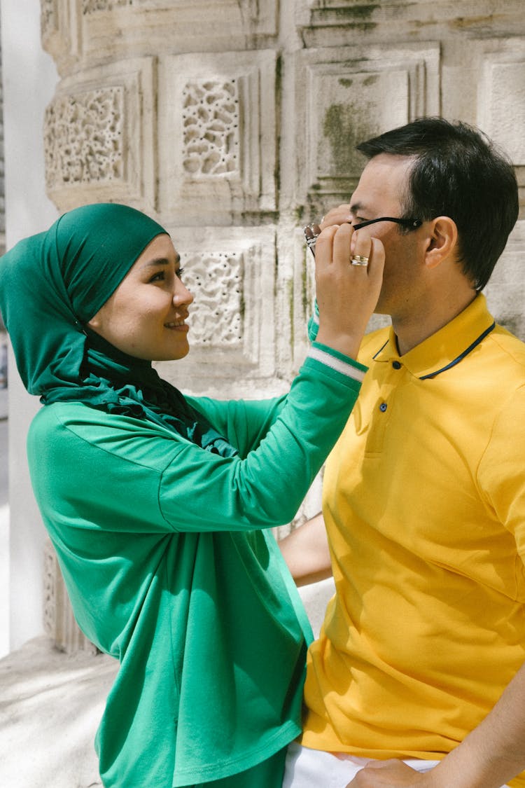 Woman In Green Hijab Removing Eyeglasses Of A Man In A Yellow Shirt