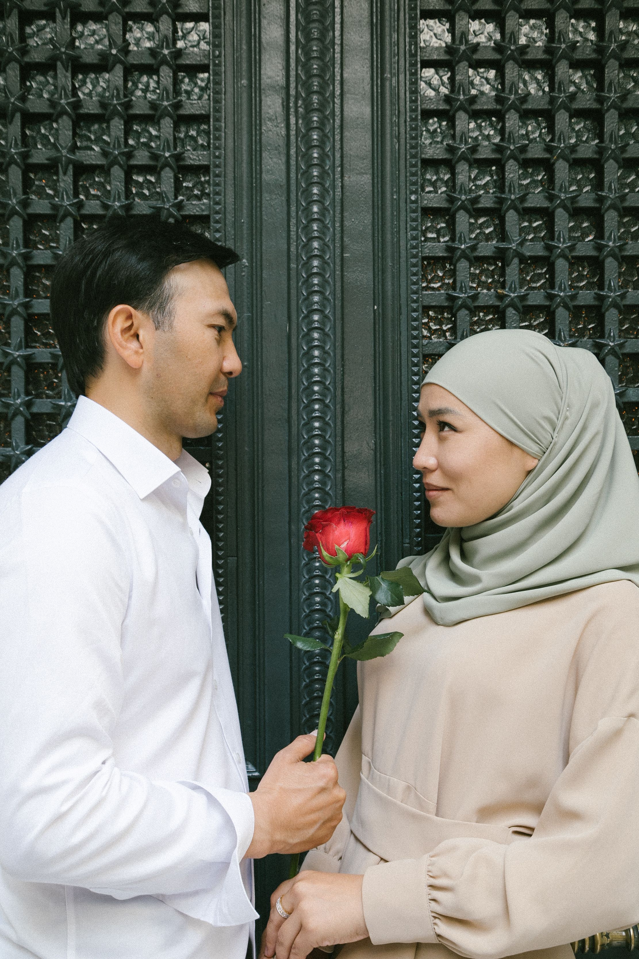A man offers a red rose to a woman in traditional attire against a decorative background in Istanbul.