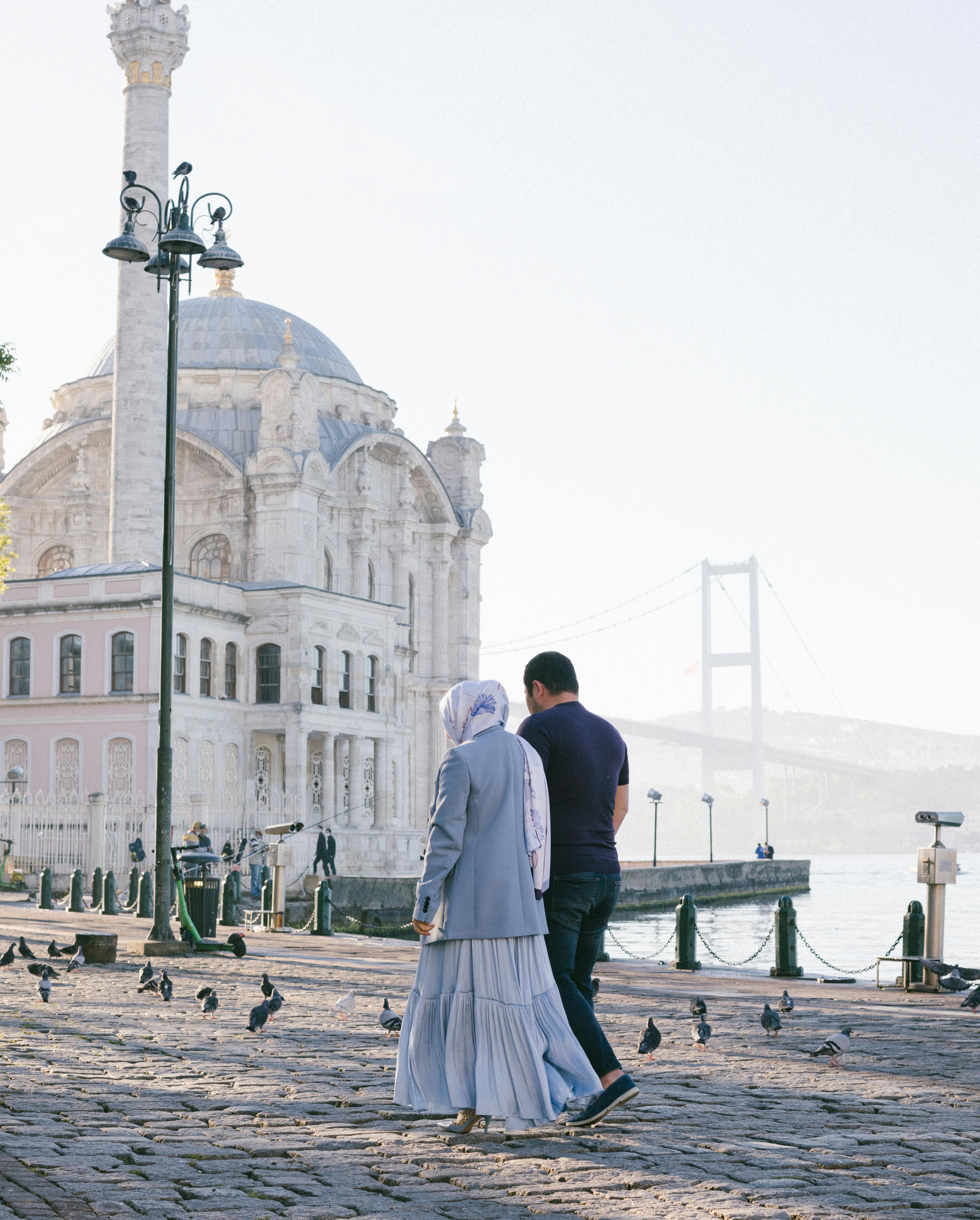 A couple walks near Ortaköy Mosque in Istanbul with a view of the Bosphorus Bridge.