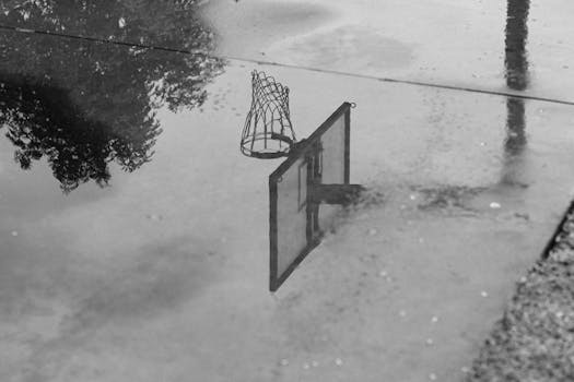 Monochromatic photo of a basketball hoop reflecting in a puddle on a court.