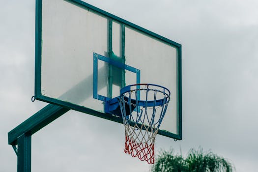 Close-up of a basketball hoop outdoors with net and backboard against a cloudy sky.