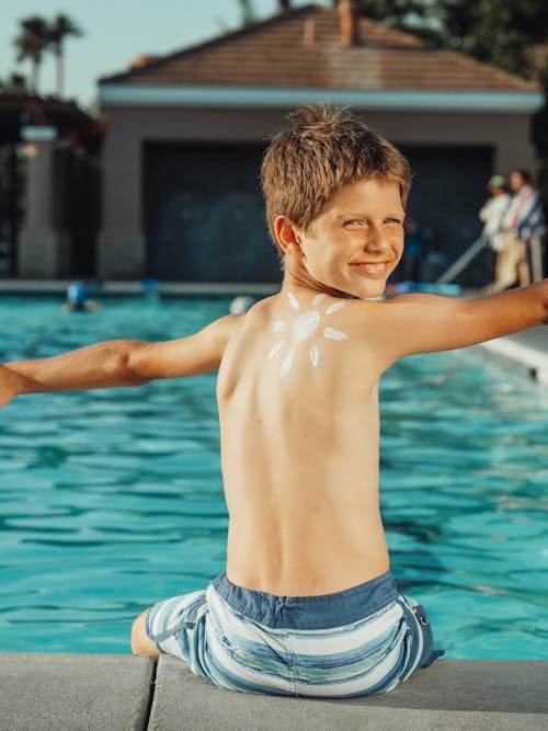 Free Boy in Blue Striped Shorts Sitting on Poolside Stock Photo