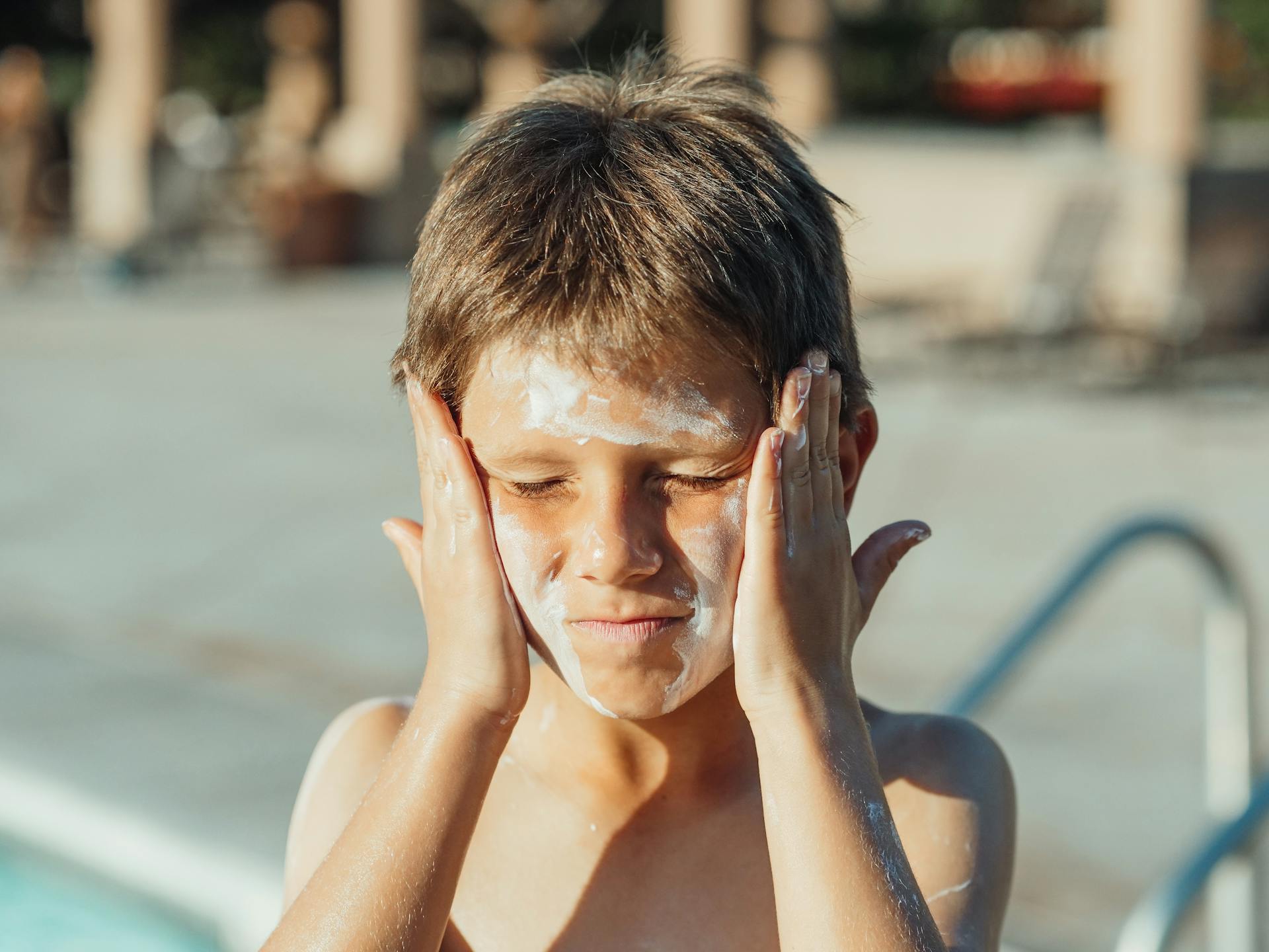 Young boy applying sunscreen cream at a sunny poolside, capturing a summer vacation vibe.