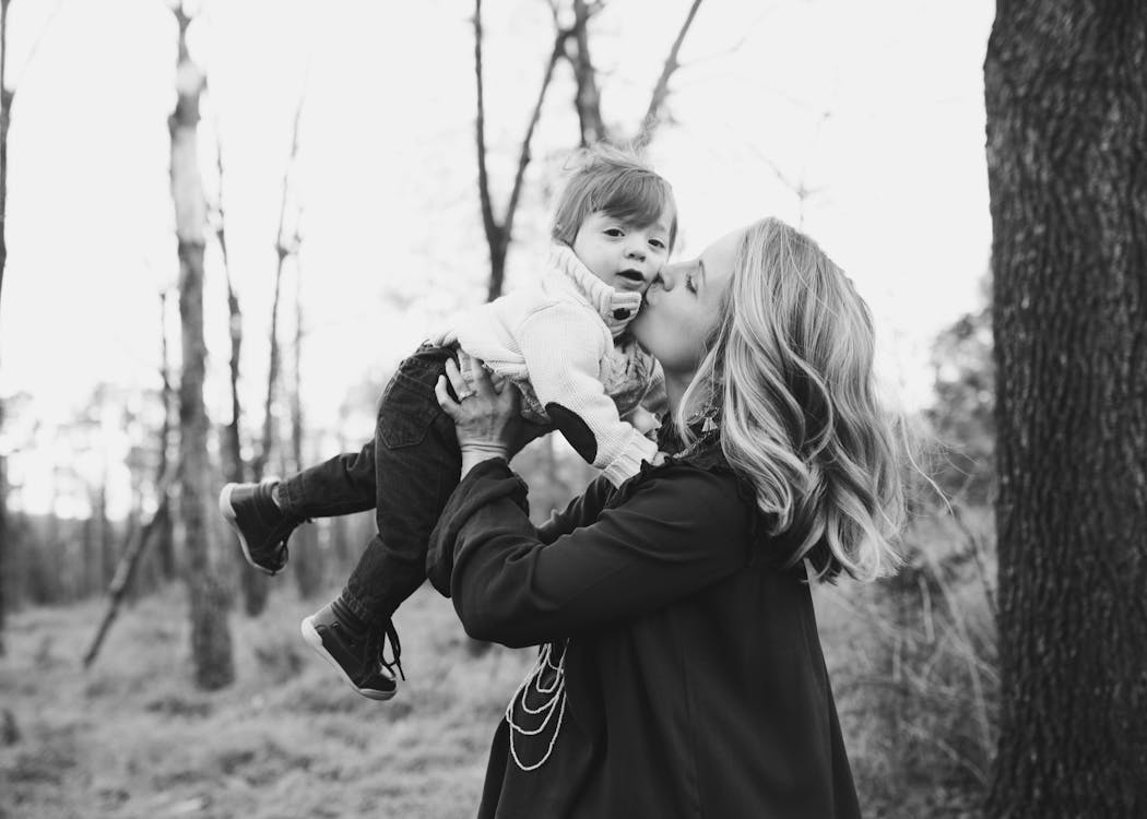 Grayscale Photo Of Woman Kissing Toddler On Cheek 