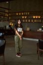 A Woman in Printed Shirt and Cargo Pants Standing Inside the Café while Looking at the Camera