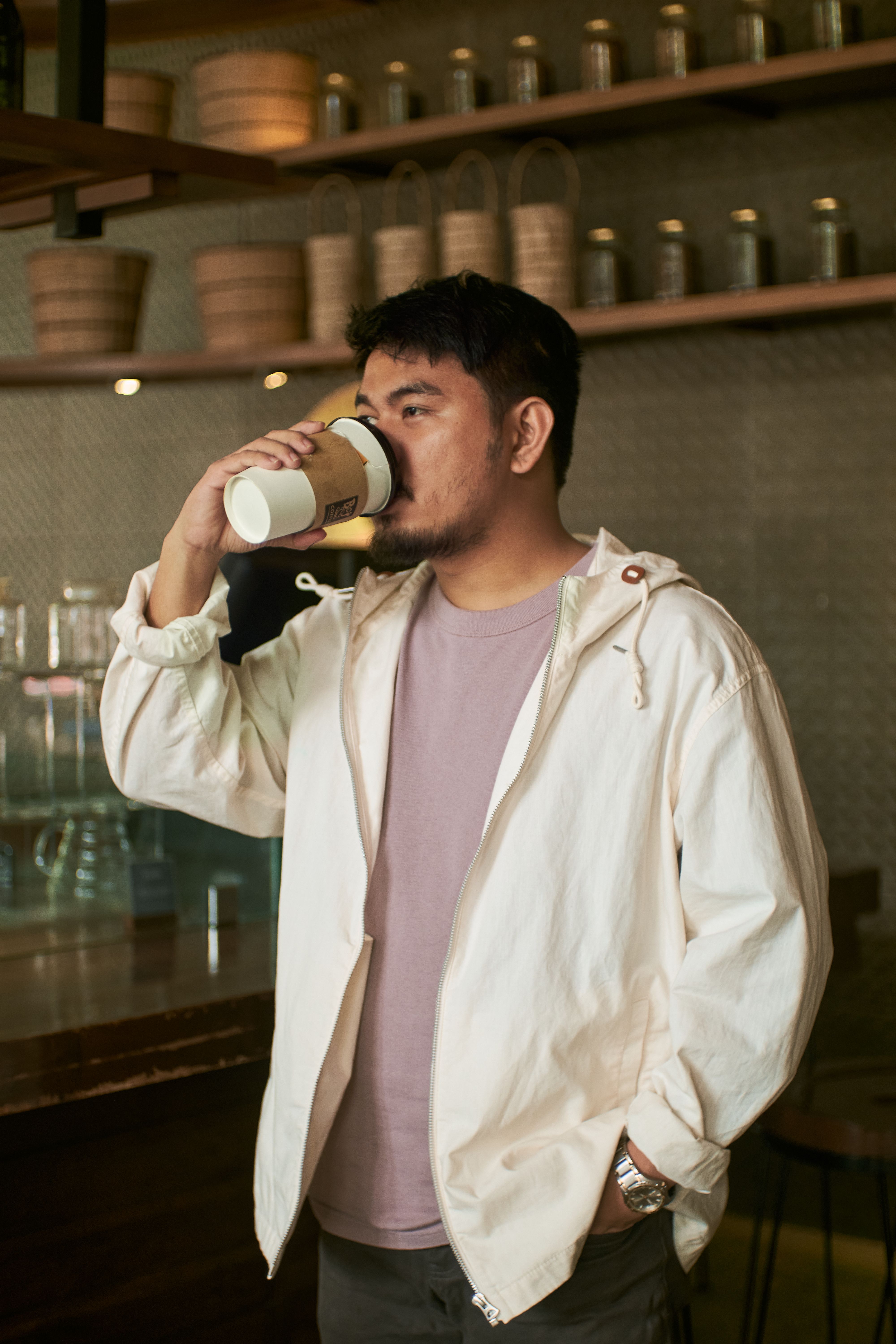 A relaxed Asian man sipping coffee in a cozy indoor cafe setting.
