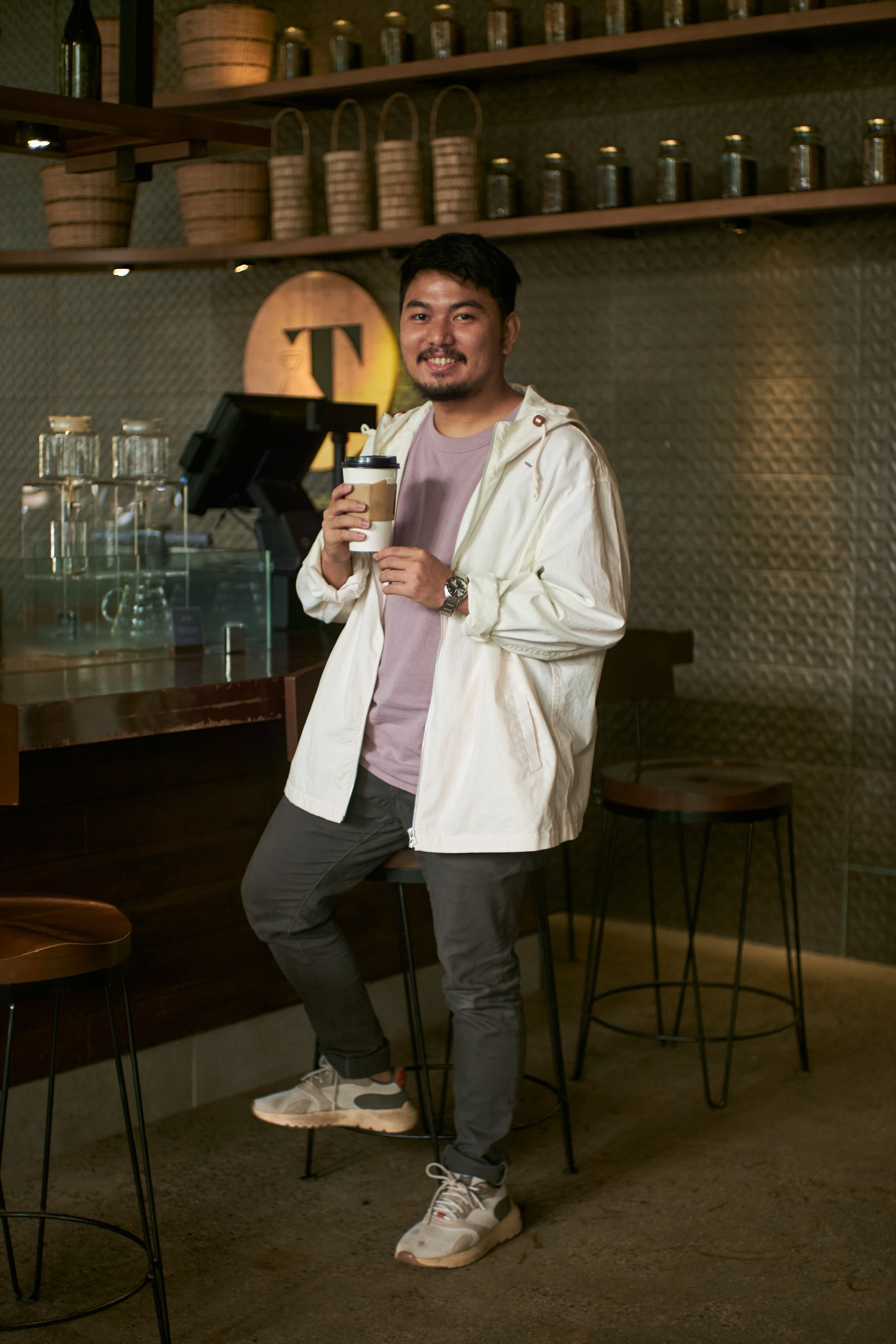 Casually dressed man holding coffee in a stylish café setting.