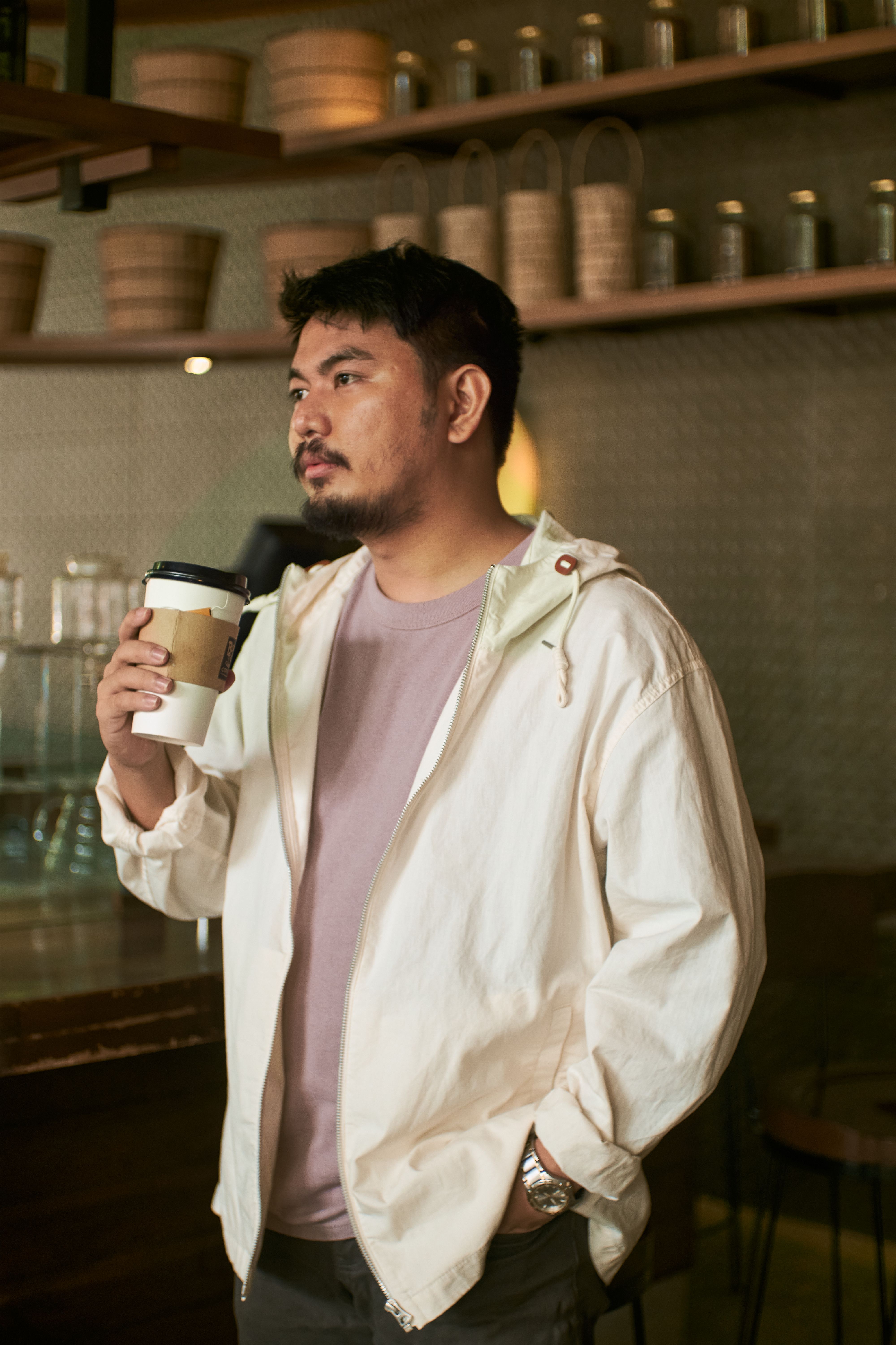 Asian man in casual attire holding coffee cup in a cozy cafe setting.