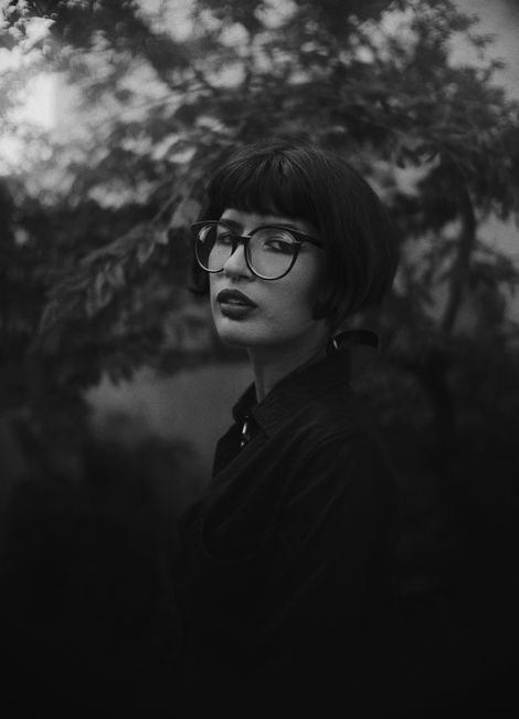Mysterious monochrome portrait of a woman outdoors with blurred foliage background.