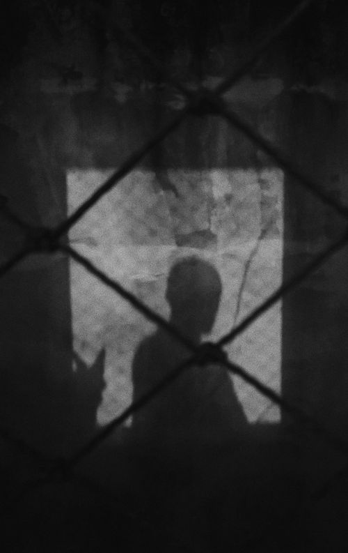 Free A shadowy silhouette behind a wire fence, capturing mystery and isolation in black and white. Stock Photo