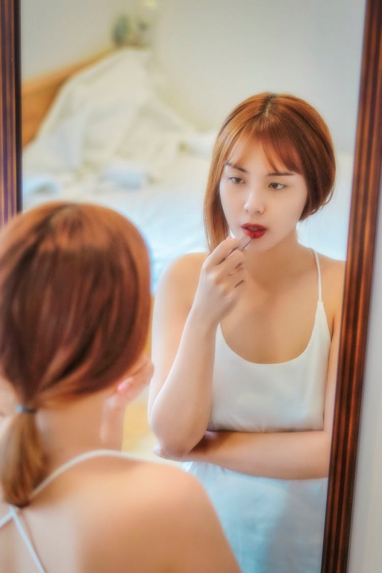 A Woman Looking In The Mirror While Putting On Lipstick