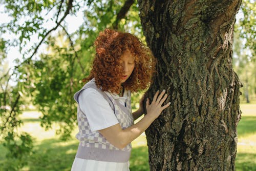 A Woman Looking Down while Holding on a Tree Trunk