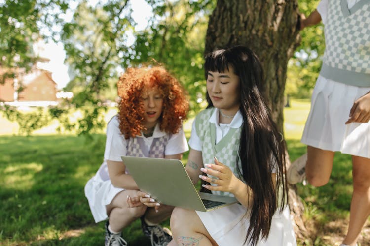 A Young Girl Holding Her Laptop While Talking To Her Friend Sitting Beside Her