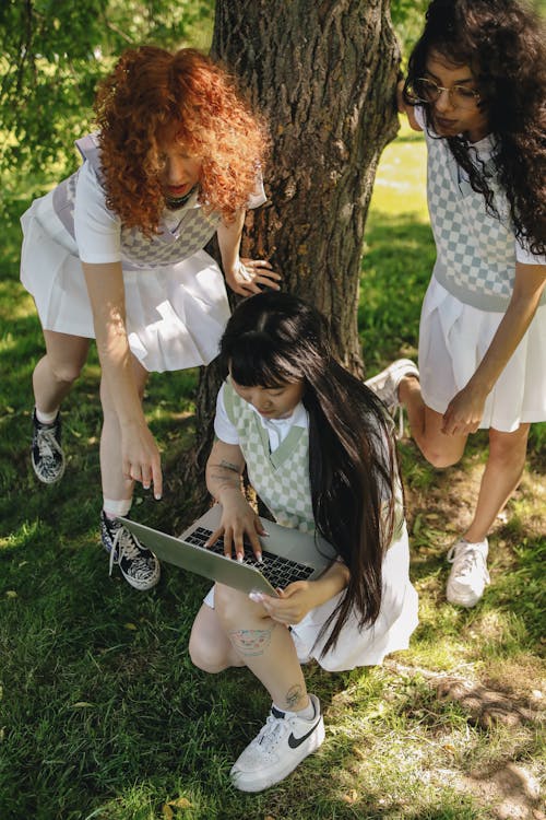 Students Looking at a Laptop while under the Shade of a Tree
