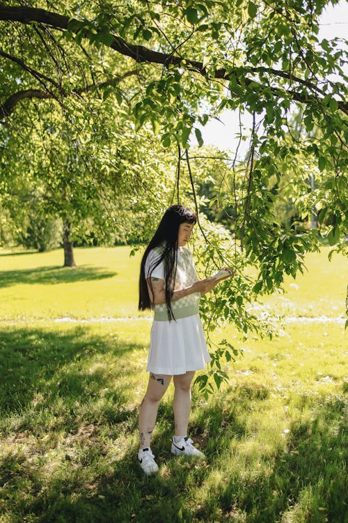 Woman in White Skirt Standing Under a Green Tree