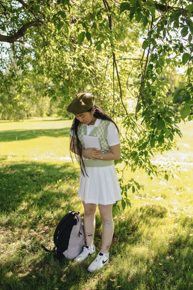 Teenage Girl In School Uniform Holding A Notebook Under A Tree