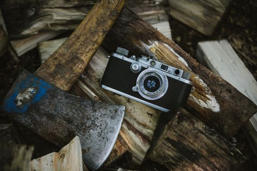 Free Classic vintage camera and weathered axe resting on a rustic woodpile, evoking nostalgia. Stock Photo
