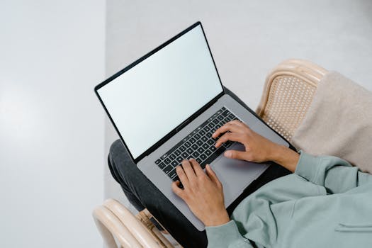 Overhead view of a person typing on a laptop in a comfortable armchair indoors.