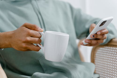 Free Close-Up Shot of a person Holding a Cup of Coffee while Using a Smartphone Stock Photo