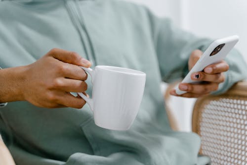 Close-Up Shot of a person Holding a Cup of Coffee while Using a Smartphone