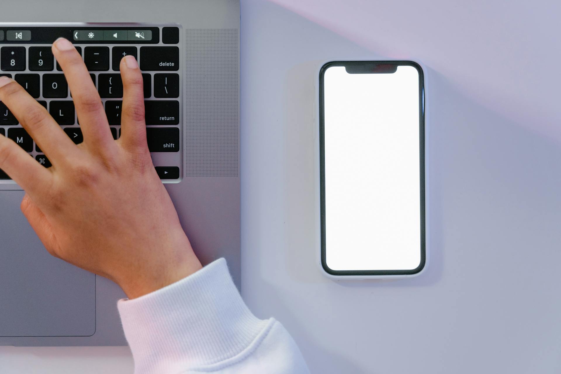 Person in White Long Sleeve Shirt Using Laptop and Mobile Phone Beside