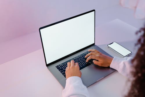 Person in White Long Sleeve Shirt Using Laptop Beside Mobile Phone 