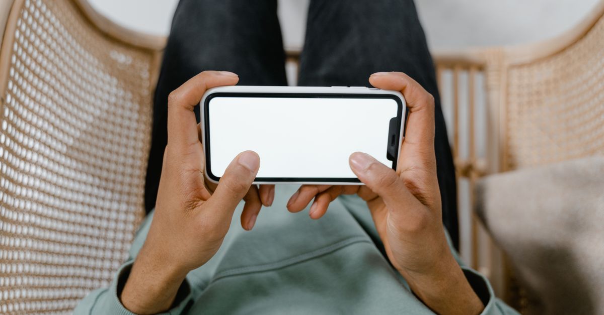 A person holding a smartphone with a blank screen while relaxing in a chair.