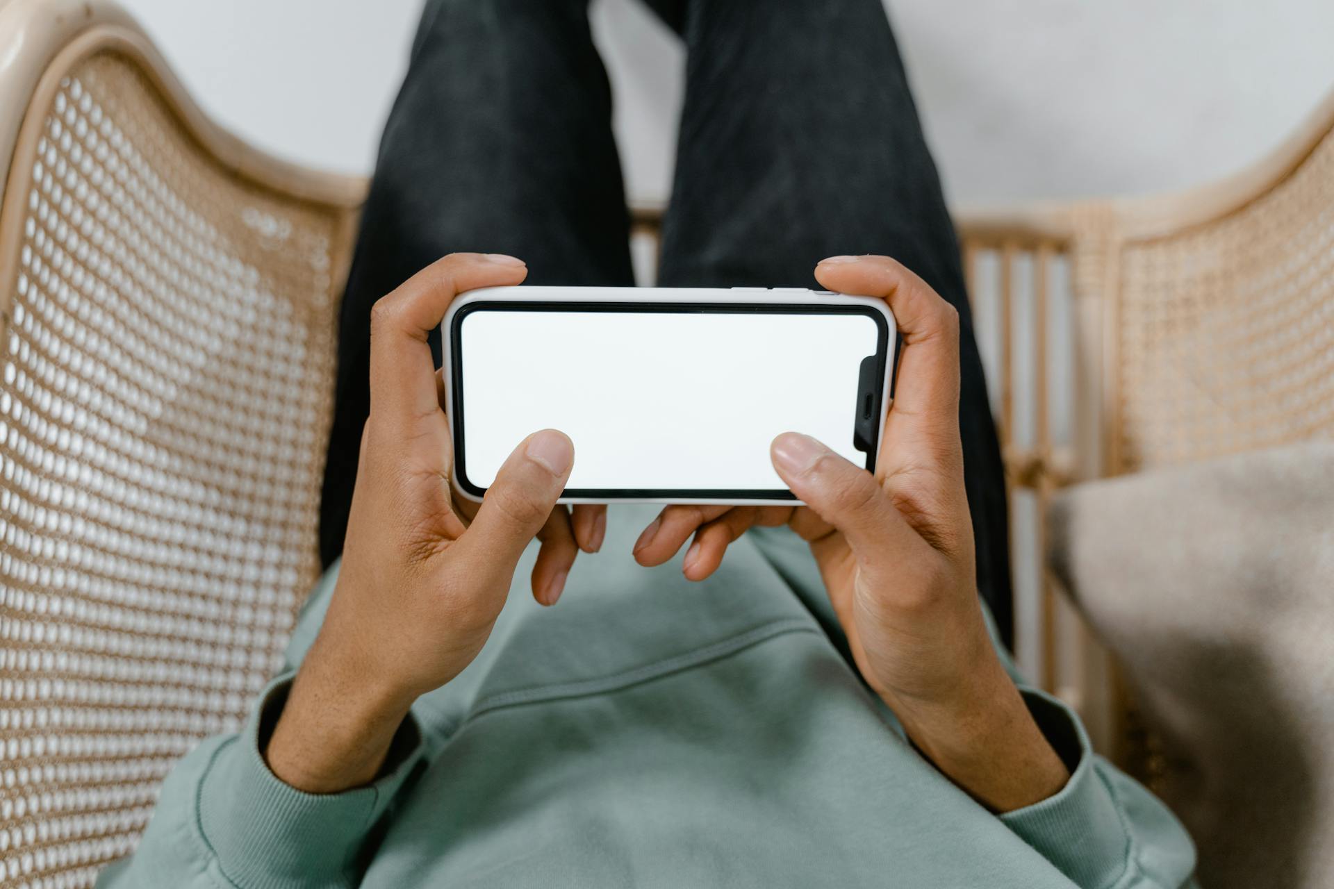 A person holding a smartphone with a blank screen while relaxing in a chair.