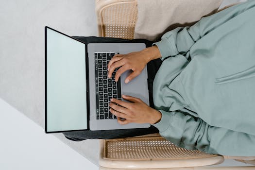 A person sitting and typing on a laptop from above, with a blank screen and casual wear.