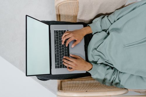 Free A person sitting and typing on a laptop from above, with a blank screen and casual wear. Stock Photo