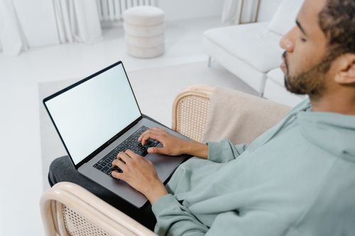 Free A man in a hoodie uses a laptop on a chair in a bright, minimalist room. Stock Photo