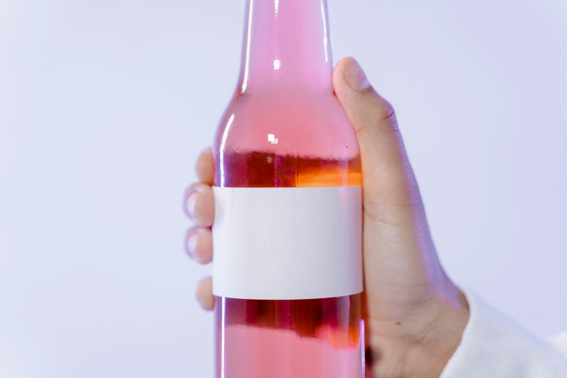 Close-up of a hand holding a pink glass bottle with a blank label for design.