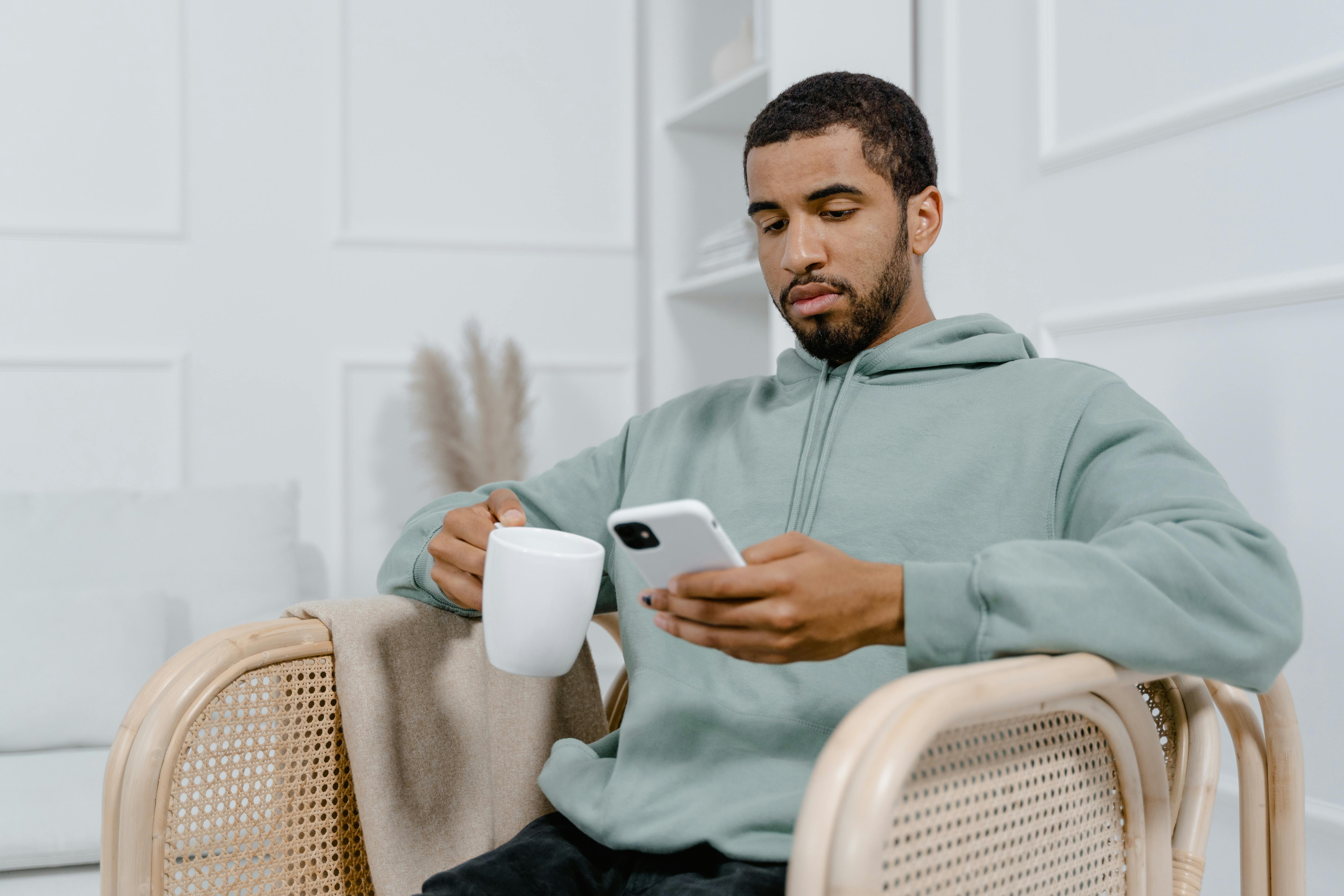 A person sitting in a sunlit living room holding a warm mug, looking out a window, no phone in sight, minimalistic decor
