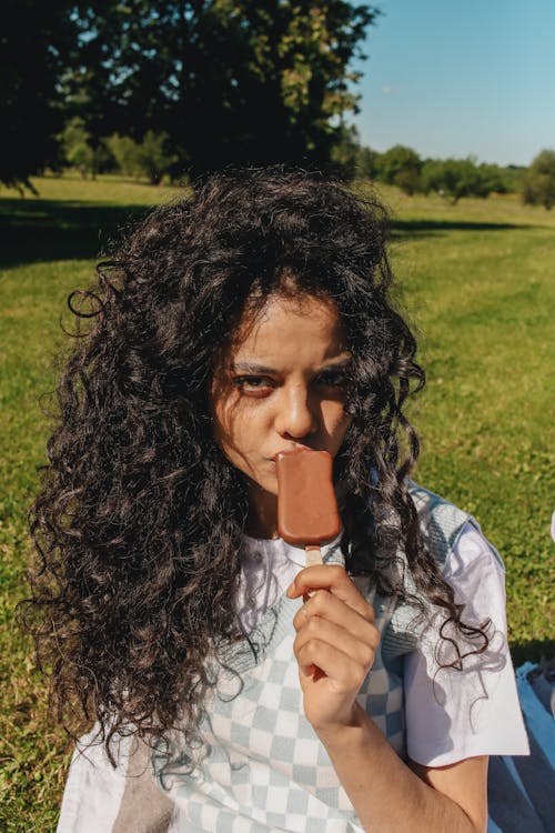 Woman with Curly Hair Eating Ice Cream in a Park