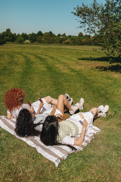 Free Three Girls Lying on Picnic Blanket on Grass Field Stock Photo