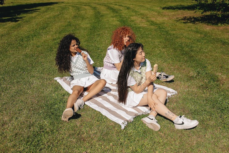 A Group Of Girls Sitting On A Picnic Blanket While Eating Ice Cream