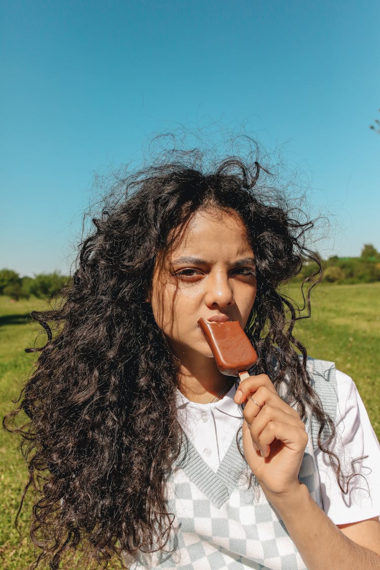 A Young Woman Eating An Ice Cream Bar At A Park