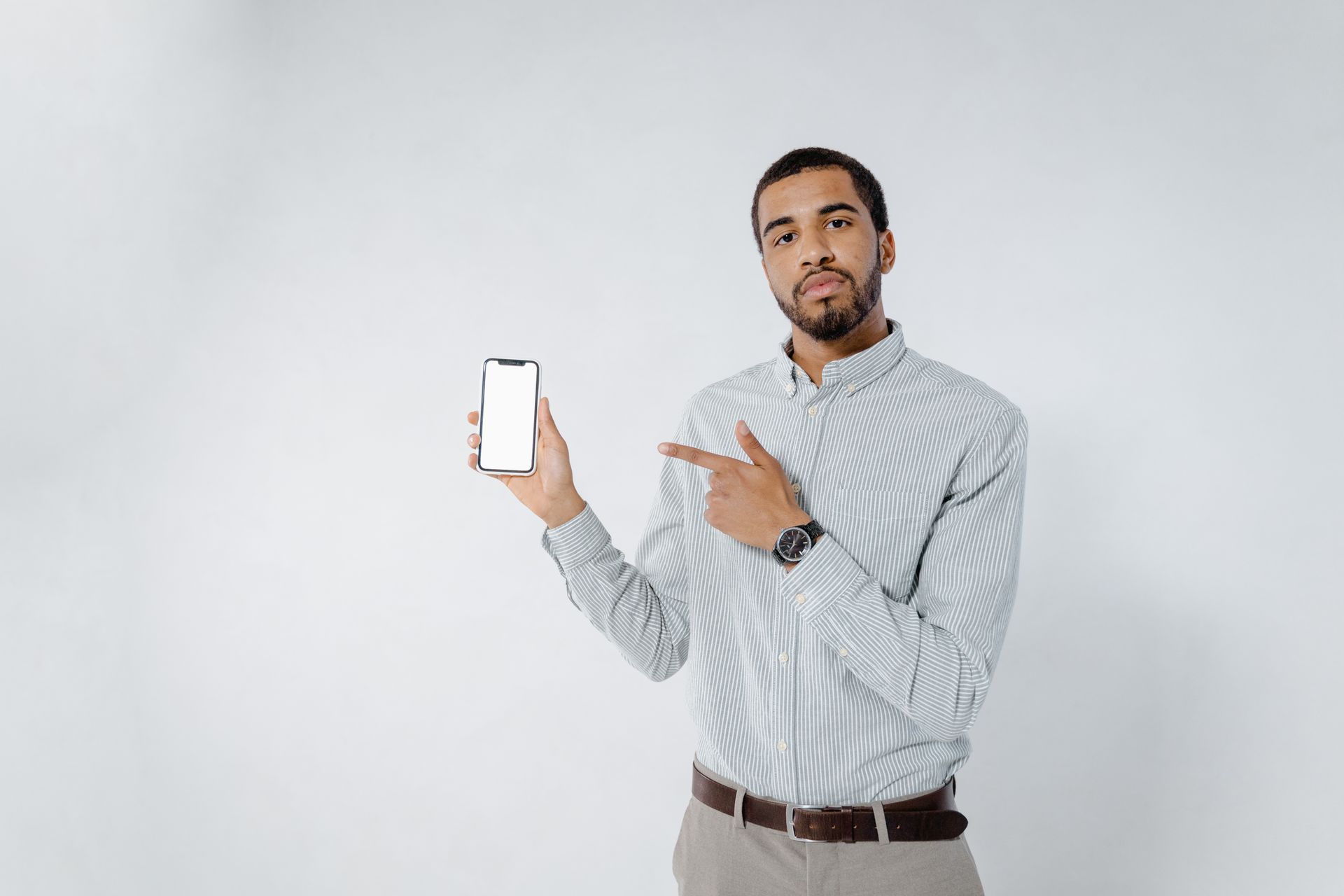 Confident young man in a striped shirt presenting a smartphone mockup with a blank screen.
