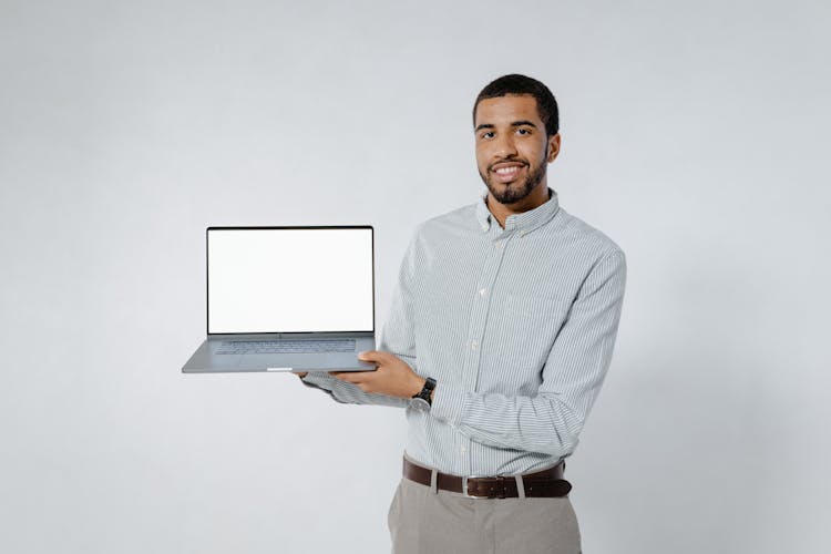 A Bearded Man In Striped Long Sleeves Holding A Laptop With White Screen