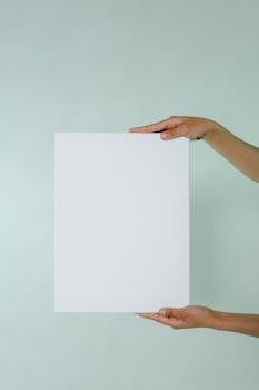 White blank card held by hands against a minimalist light green background for mockup usage.