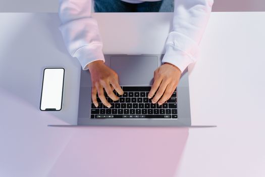 Hands typing on a laptop beside a smartphone on a minimalist desk.