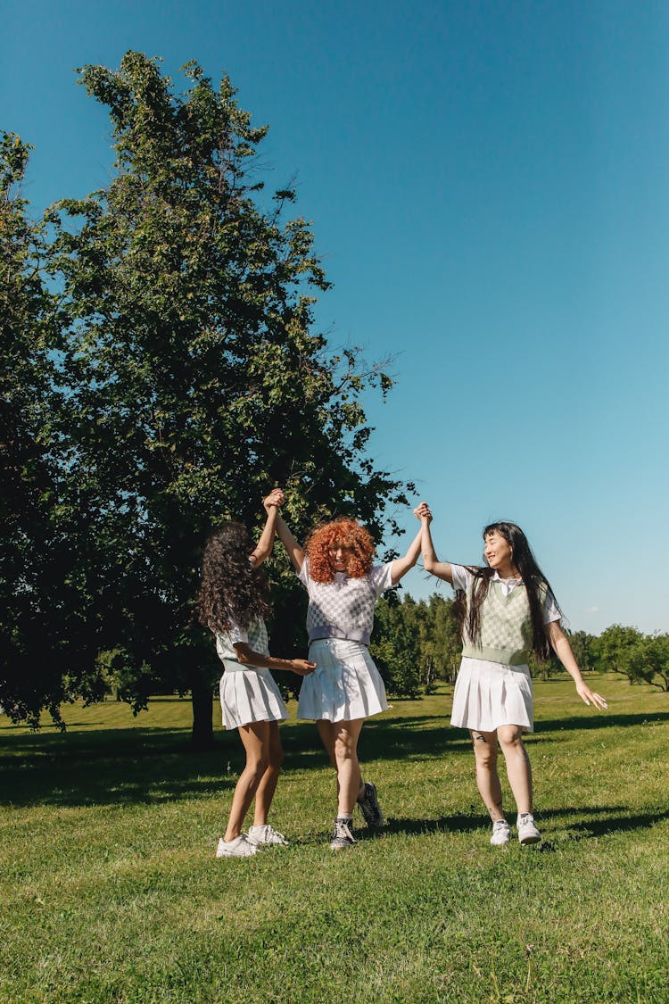 Three Young Women Dancing On Grass Field