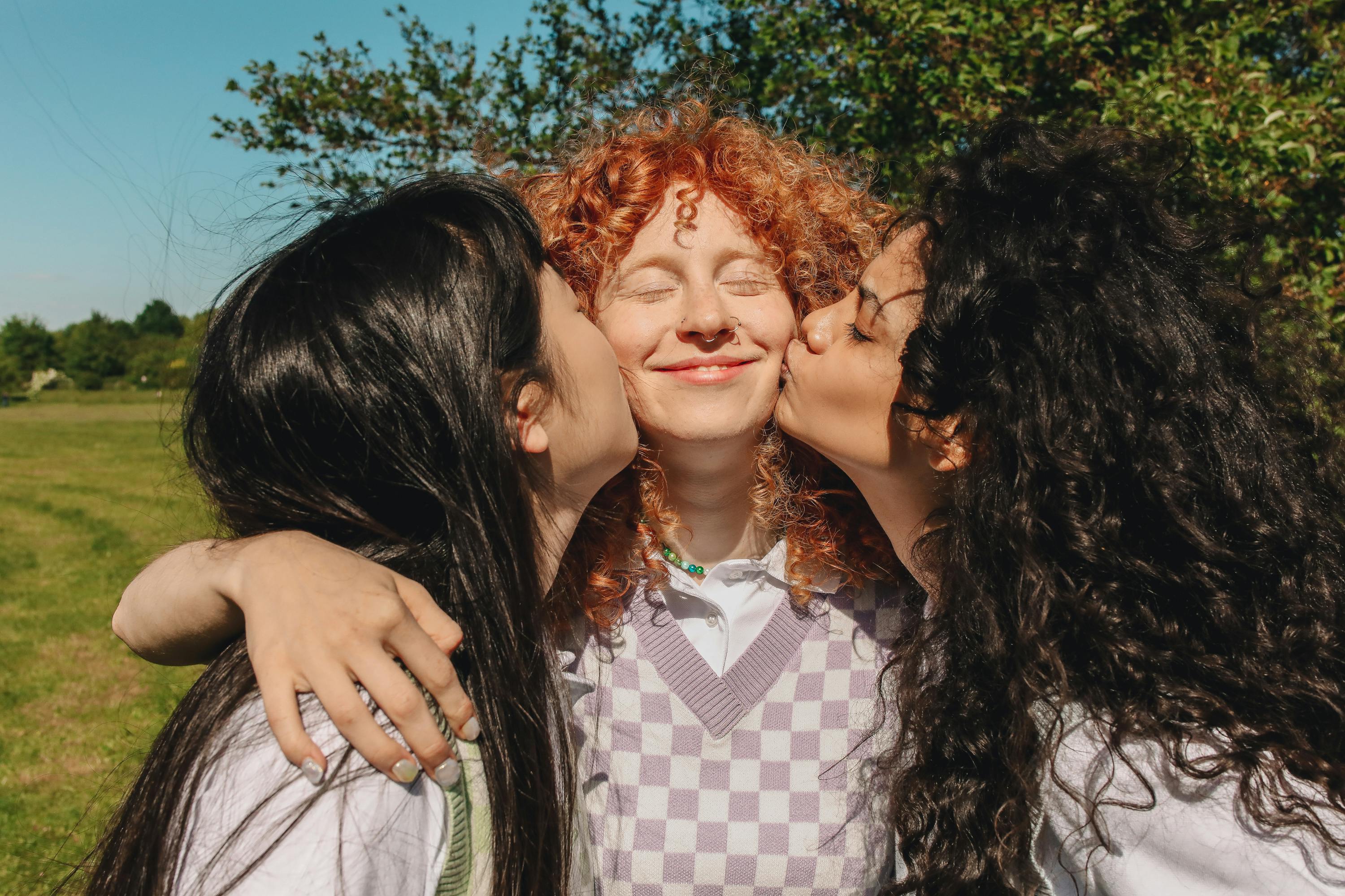 photograph of girls kissing their friend on the cheek