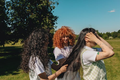 Two Young Women Doing Friend's Hair on Grass Field