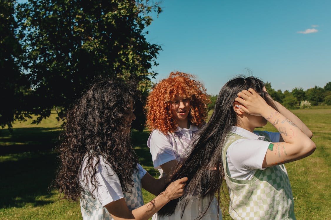 Two Young Women Doing Friend's Hair on Grass Field