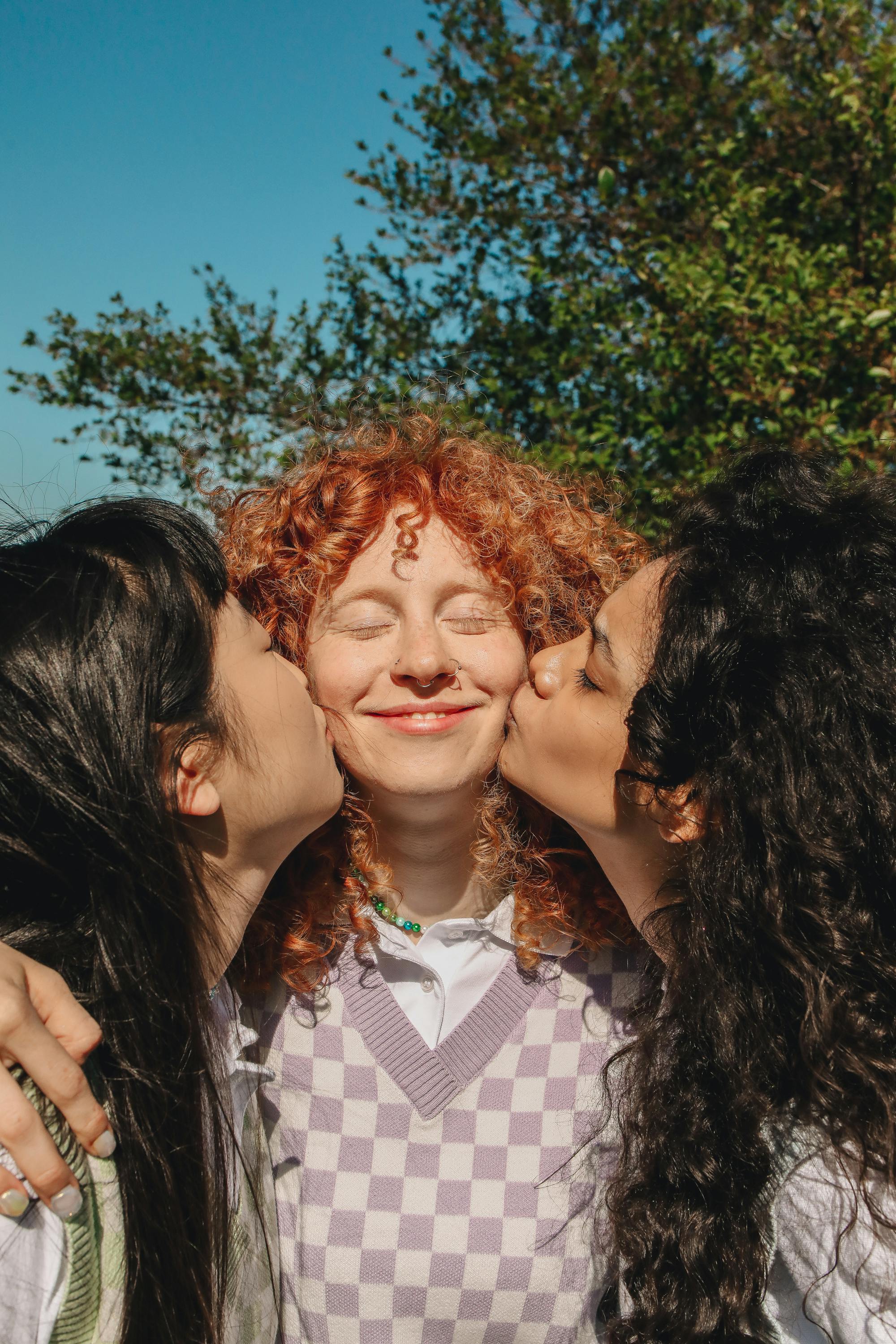 two girls kissing cheeks of their friend