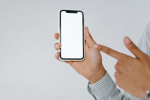 Detailed image of a person holding and pointing at a smartphone with a blank screen, perfect for mockup use.