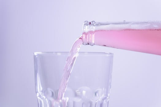 Close-up of pink beverage being poured from a bottle into a clear glass with a white background.