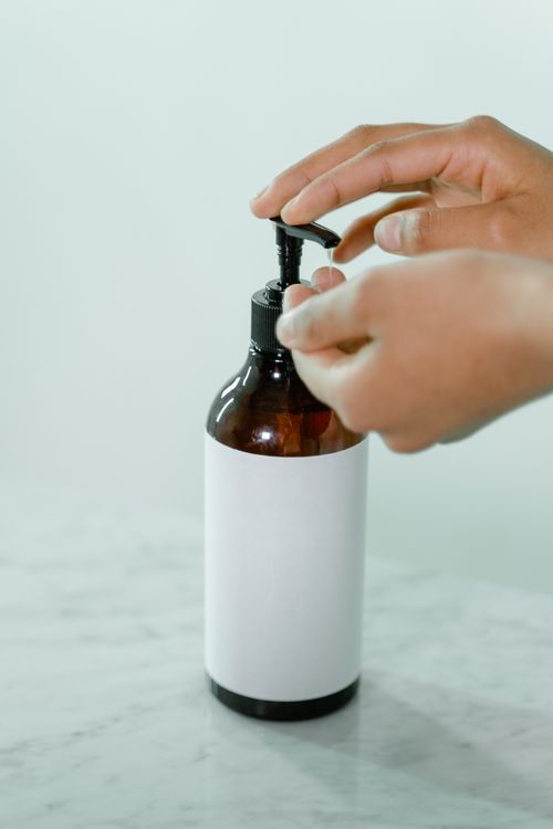 Free Close-up of hands dispensing a product from a brown bottle with pump on marble surface. Stock Photo