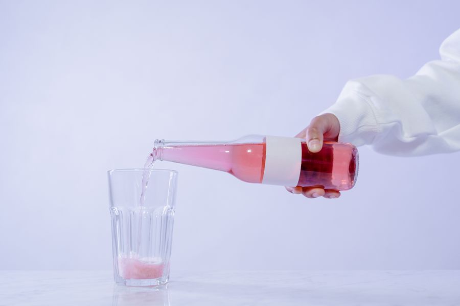 A close-up of a hand pouring a pink drink from a bottle into a glass.